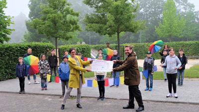 Foto AMK: Stephanie Henning, Konrektorin der Regenbogen-Schule, mit den Kindern der Klasse 4a und Marcus Berghaus, Geschäftsführer der AMK, auf dem Hof der Schule. Im Hintergrund, mit Regenschirmen, die Lehrkräfte von li. nach re.: Helena Franke, Jens Faber und Karin Futter